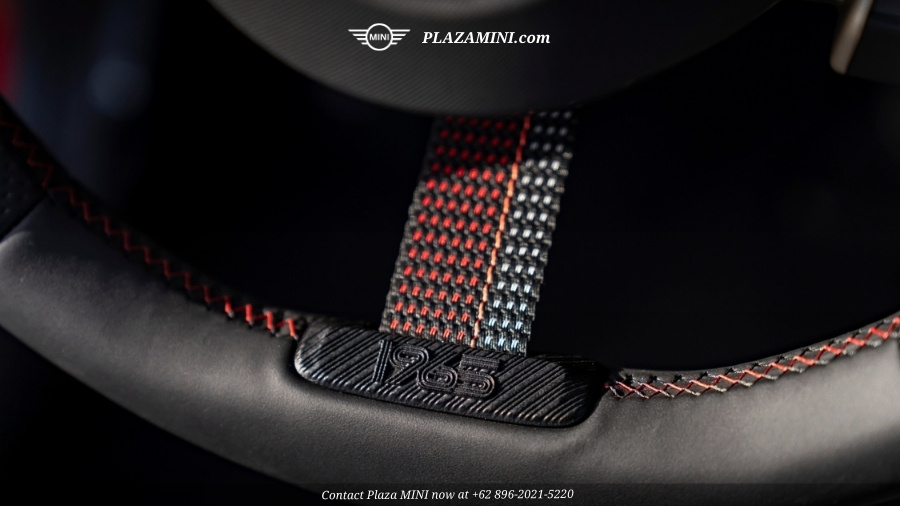 A close-up, high-angle shot of the interior door sill of a red MINI Cooper. The black door sill protector features a stylized "1964" graphic in white and red, alongside the text "VICTORY EDITION." Part of the black leather car seat with red stitching and electronic adjustment buttons is visible in the background.
